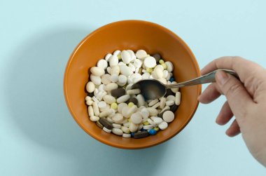 Bir el bir kaseden ilaç topluyor. Kaşıkla ilaç. Mavi arka planda ilaçlı plaka.