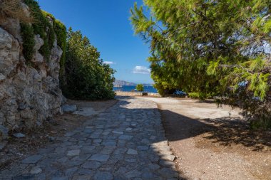 Hydra 'nın arka planında bitki örtüsü ve okyanus olan yürüyüş yolu