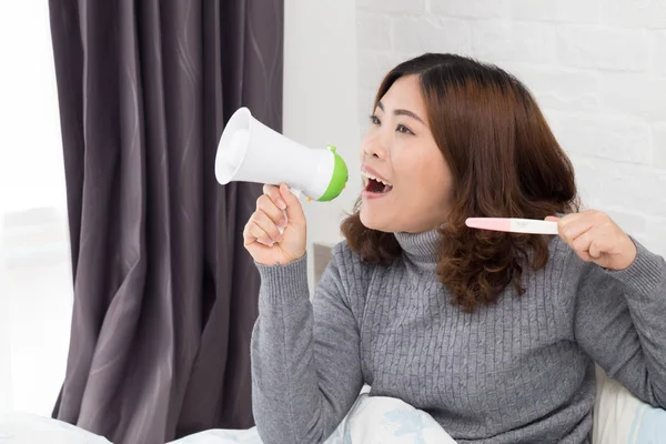 Happy asian woman holding megaphone and pregnancy test — Stock Photo, Image