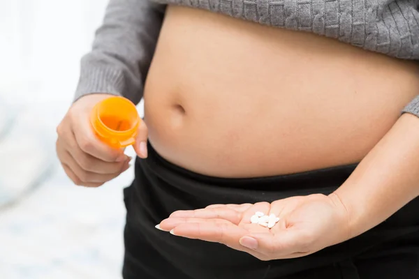 Barriga de mulher grávida e pílulas de vitamina na mão — Fotografia de Stock