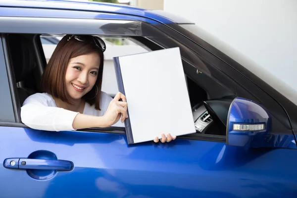 Happy Asian kobieta gospodarstwa samochód ubezpieczenia książki i siedzi w samochodzie — Zdjęcie stockowe