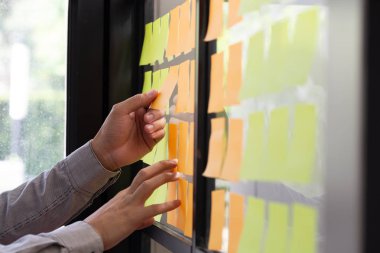 IT worker tracking his tasks on kanban board. Using task control of agile development methodology. Man attaching sticky note to scrum task board in the office clipart