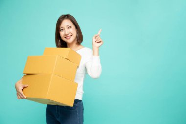 Happy Asian woman holding package parcel box and pointing  finger to empty copy space isolated on light green background clipart