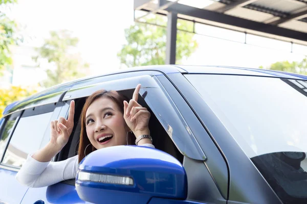 Mujer asiática feliz sentado en el coche y apuntando hacia el espacio de copia vacío en el techo del coche superior — Foto de Stock