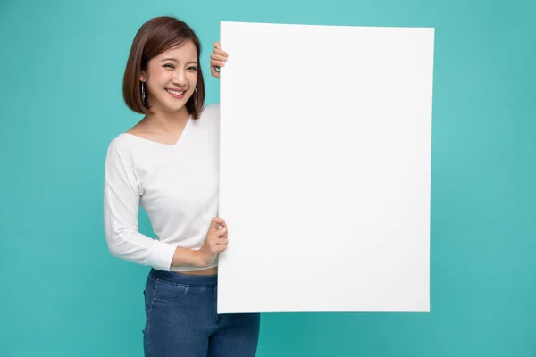 Sonriente mujer asiática feliz sosteniendo y de pie detrás de un gran cartel blanco aislado sobre fondo verde claro —  Fotos de Stock