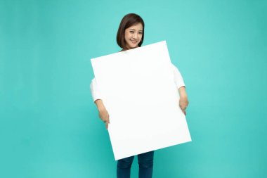 Gülümseyen mutlu Asyalı kadın açık yeşil arka planda izole edilmiş büyük beyaz posteri tutuyor ve arkasında duruyor.