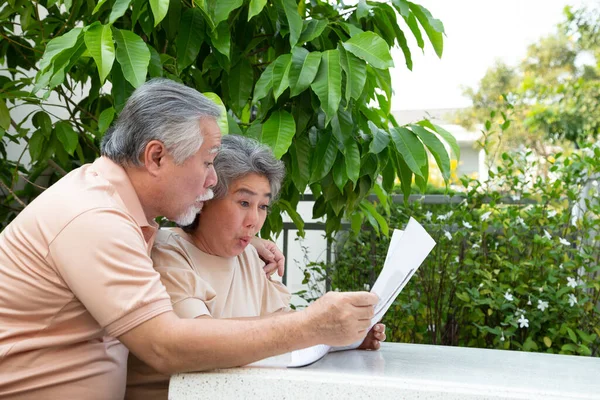 Excited Asian senior mature couple feeling amazed by good surprise news while reading newspaper or magazine at front garden home