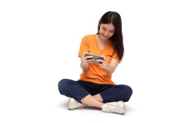Genç Asyalı kadın beyaz arkaplanda izole edilmiş akıllı telefon oyunu uygulaması kullanırken ifade ve yerde oturmak