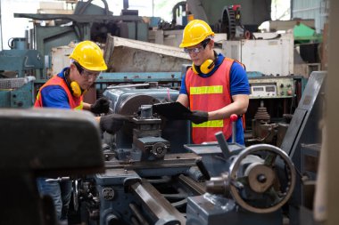 Sarı şapkalı Asyalı fabrika mühendisi makineyi kontrol ediyor. Yıllık bakım konsepti.