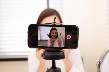 Asyalı kadın güzellik blogcusu veya blogcu cep telefonu ve sosyal medya kanalı veya web sitesinde kozmetik makyaj öğretim videosu canlı yayını, Nüfuzlu Yaşam tarzı ve fotoğraf çekerken özçekim