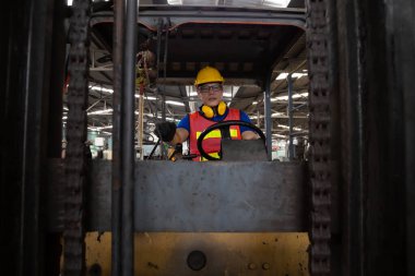 Fabrikada çalışan Asyalı forklift sürücüsü kameraya bakıyor.