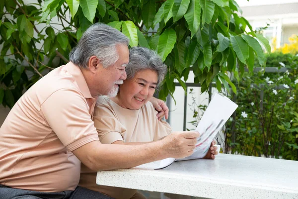 Asiatisk Senior Par Griner Mens Læser Avis Bordet Udendørs Forhaven - Stock-foto