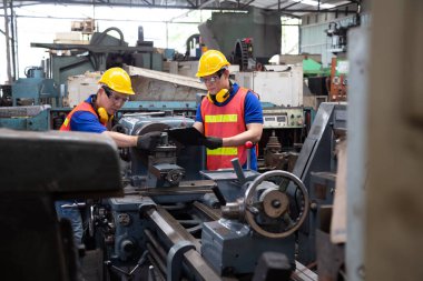 Sarı şapkalı Asyalı fabrika mühendisi makineyi kontrol ediyor. Yıllık bakım konsepti.