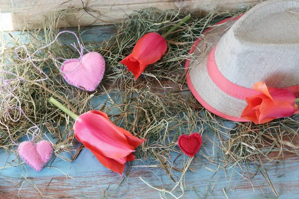 Fresh tulips, hearts decor, straw hat, hay on a wooden surface, top view