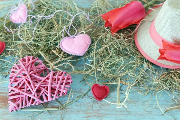 Fresh tulips, hearts decor, straw hat, hay on a wooden surface, top view