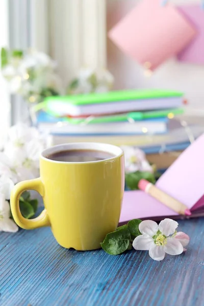 Bir fincan kahve, notlar için boş bir defter, bir yığın kitap, ahşap pencere eşiğinde elma çiçekleri, ev konforu konsepti