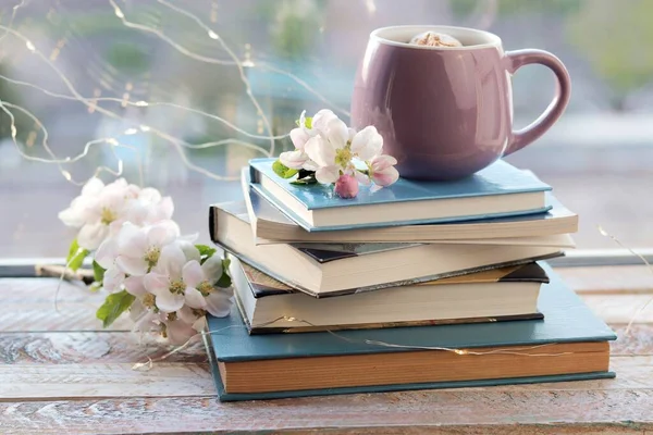 Bir fincan kahve, bir yığın kitap, ahşap pencere eşiğinde elma çiçekleri, ev konforu   