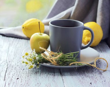 Büyük bir fincanda sıcak çay, taze papatya çiçekleri, organik limonlar, ahşap pencere eşiğinde elmalar, ev konforu