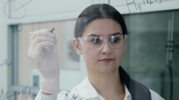 Mujer en laboratorio escribir fórmula en el tablero de vidrio — Vídeo de stock