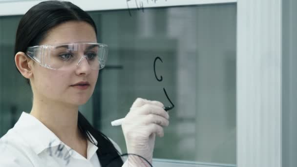 Frau im Labor schreibt Formel auf Glastafel — Stockvideo