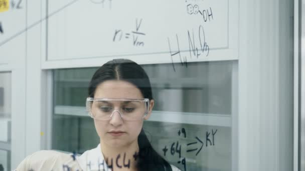 Frau im Labor schreibt Formel auf Glastafel — Stockvideo