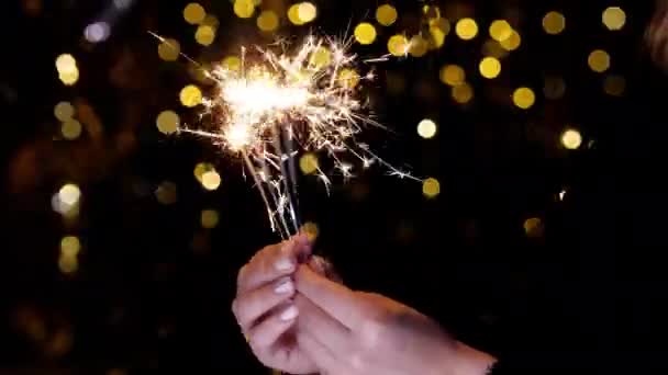 The burning sparkler flashes brightly in hands and the golden sparks fly apart. — Stock Video