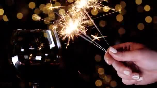 Sparkler brandt in zijn handen, en daarnaast staat een knipperend glas wijn. — Stockvideo