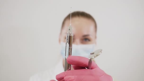 Maszkos női fogorvos fogászati eszközökkel a kezében és a gyógyszer fecskendőből történő felszabadítása — Stock videók