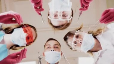 Masked faces of team of doctors over patient with dental tools in hands pov