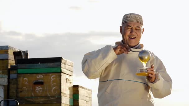 Портрет старого азиатского фермера или улыбающийся старшеклассник наливает мед в контейнер — стоковое видео