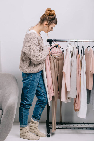 side view of girl standing near stand and choosing what to wear 