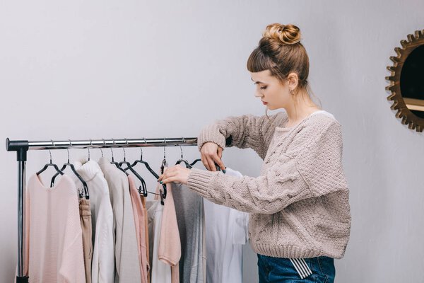 side view of girl standing near stand and choosing what to wear 