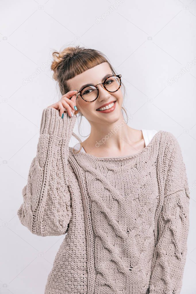 smiling girl standing and touching glasses isolated on white