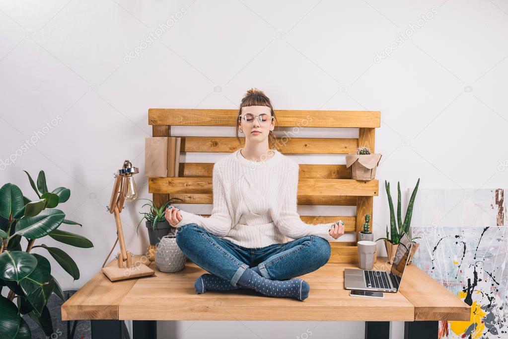 girl sitting in office in yoga pose with closed eyes