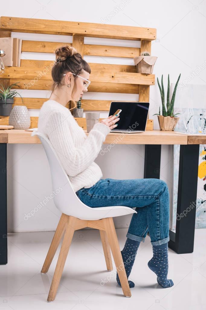 side view of girl sitting on chair in office and using smartphone