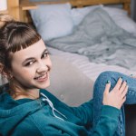 Smiling girl sitting on armchair in bedroom and looking at camera