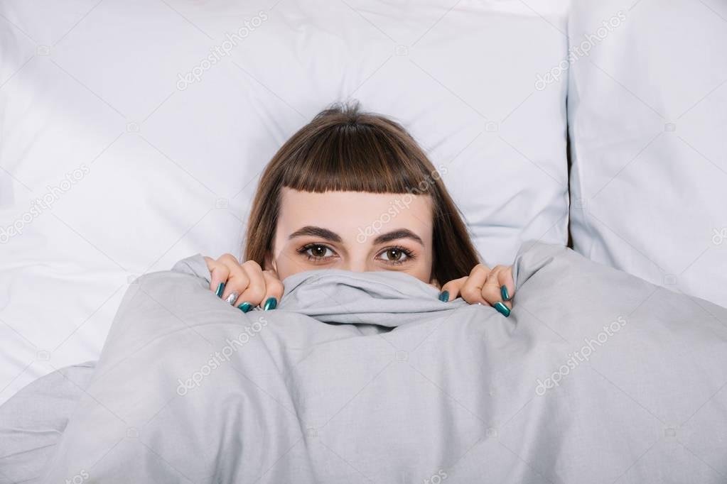 girl looking out from blanket in bedroom