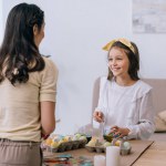 Happy little daughter painting easter eggs together with mother