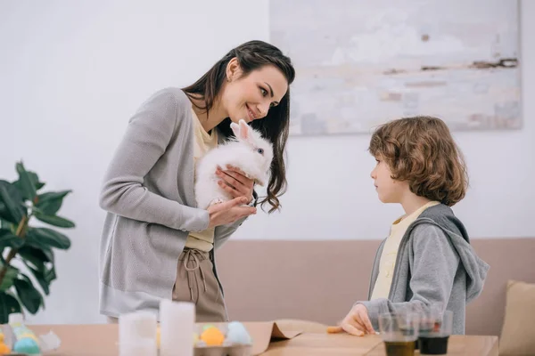 Madre Mostrando Conejo Blanco Hijo Mientras Pintando Huevos Pascua — Foto de Stock