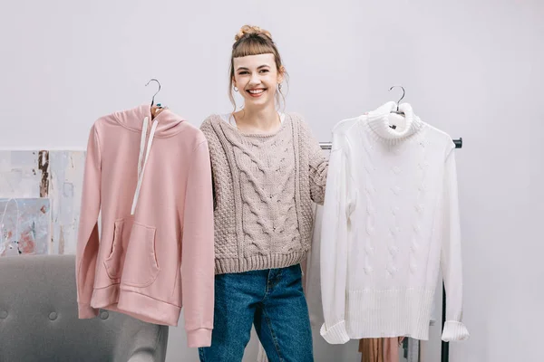 Lächelndes Mädchen im Stehen mit Kleiderbügeln und Pullovern — Stockfoto