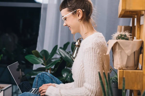 Seitenansicht eines lächelnden Mädchens, das mit Laptop auf dem Tisch im Büro sitzt — Stockfoto