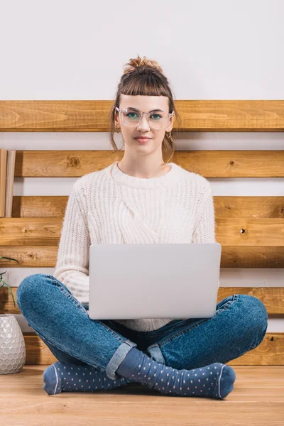 Girl sitting on table in office with laptop and looking at camera — Stock Photo