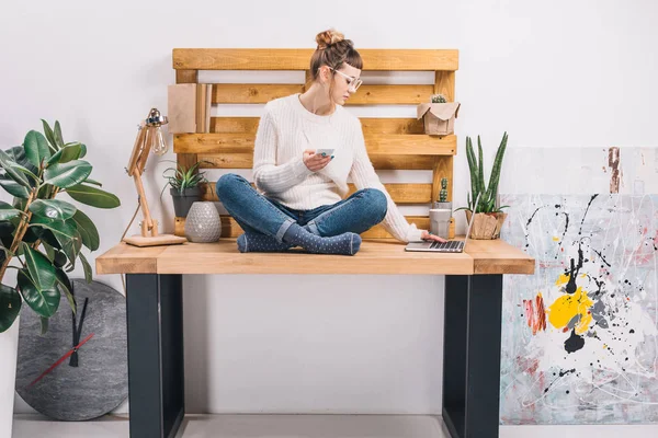 Girl sitting on table in office and looking at laptop — Stock Photo