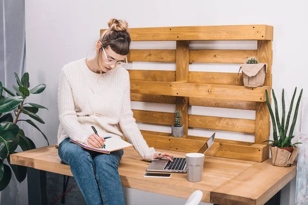 Mädchen sitzt auf Tisch im Büro und schreibt etwas ins Notizbuch — Stockfoto