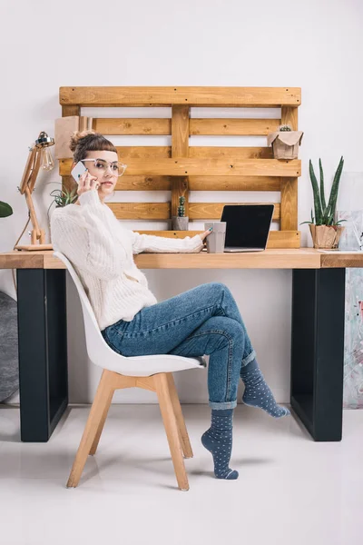 Girl talking by smartphone in office and holding cup — Stock Photo