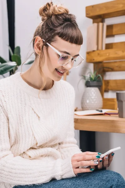 Smiling girl sitting on chair and looking at smartphone in office — Stock Photo