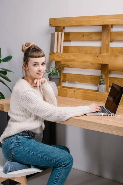 Chica trabajando con el ordenador portátil en la oficina moderna y mirando a la cámara - foto de stock