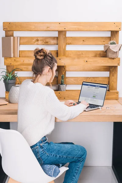 Chica sentada en la mesa con el ordenador portátil con cargado página de Facebook - foto de stock