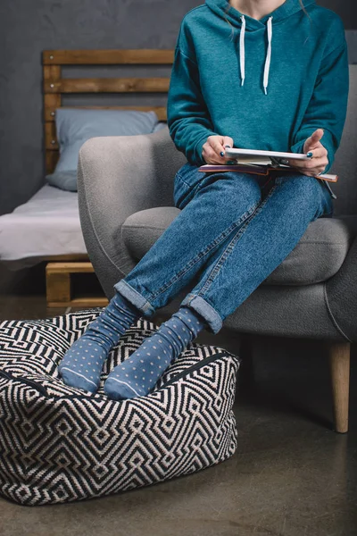 Imagen recortada de niña sentada en el sillón y sosteniendo la tableta en las manos - foto de stock