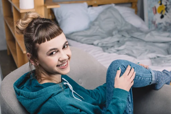 Sorrindo menina sentada na poltrona no quarto e olhando para a câmera — Fotografia de Stock